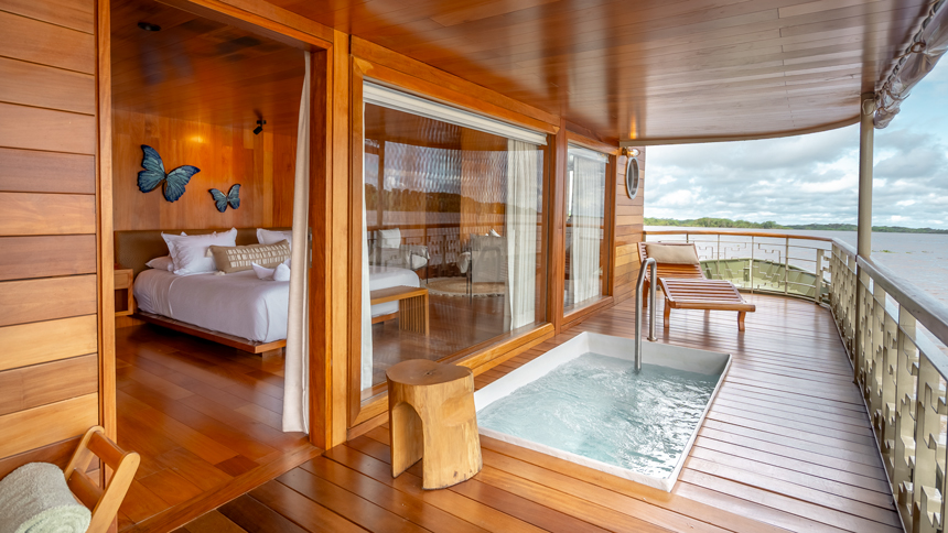 Luxury boat charter cabin with large floor-to-ceiling windows, and a small hot tub on a private wooden deck overlooking the Amazon