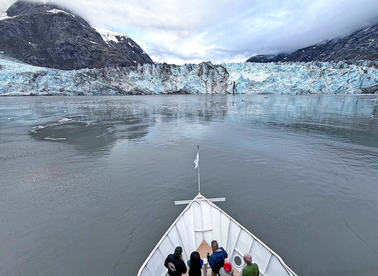 A group of travelers gather at the bow of a ship as it closely approaches the face of a glacier in Glacier Bay National Park, Alaska. 