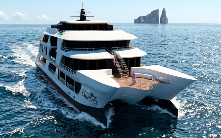 Rendering of white & black mega-catamaran Eminence cruising past sunny Kicker Rock in Galapagos, with woman standing on deck.