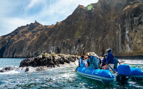Small blue dinghy with Eminence Galapagos cruise guests pulls up beside rock to view wildlife on a sunny day.